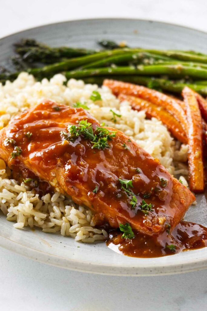 Salmon and marsala sauce on a dinner plate with rice and veggies.