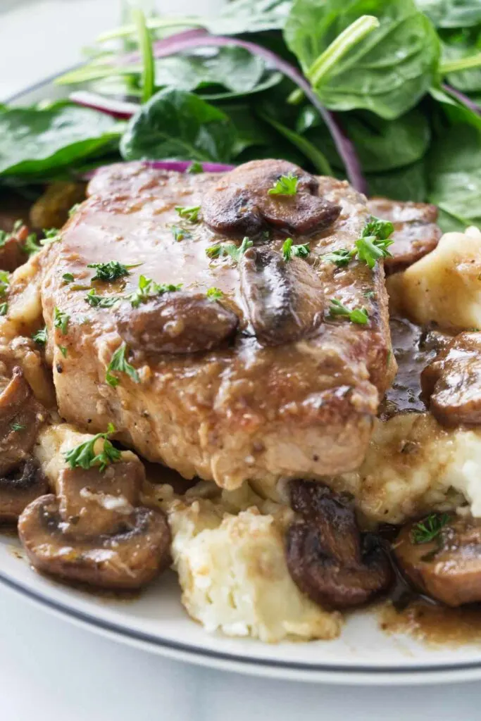 A pork chop with marsala sauce on a bed of mashed potatoes.