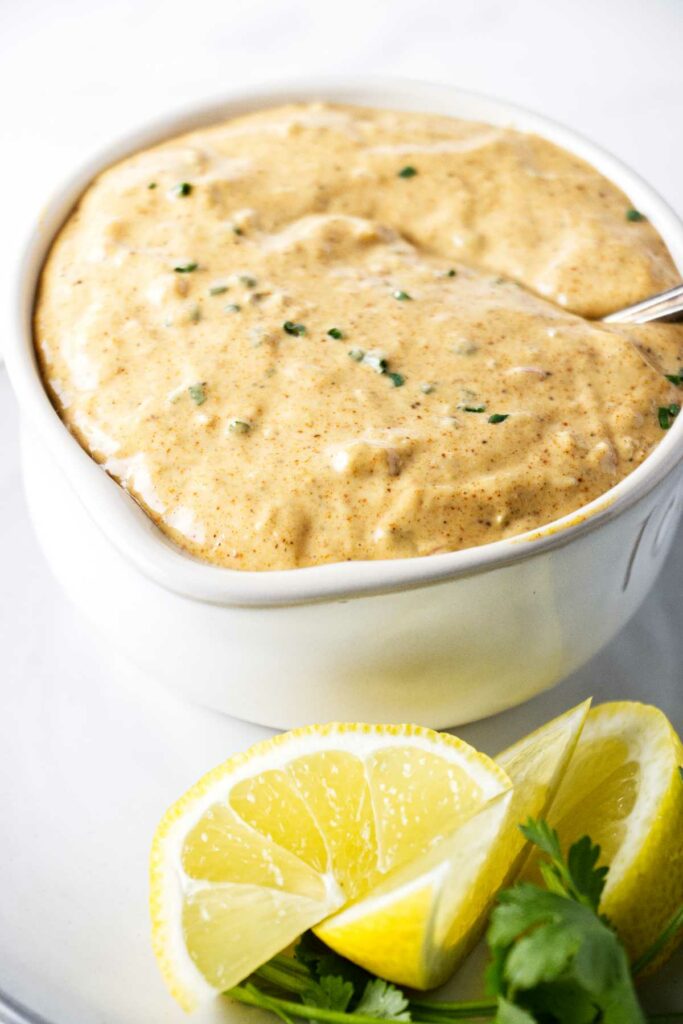 A dish of creamy remoulade sauce next to lemon slices.