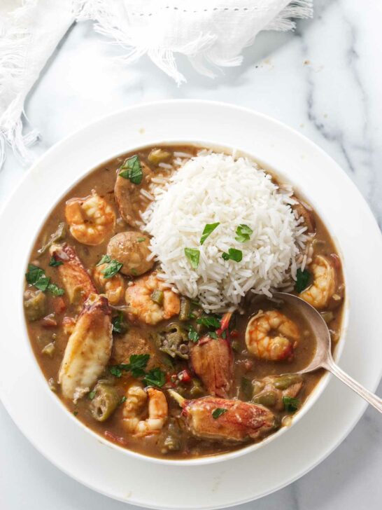 A bowl of seafood gumbo with a scoop of rice on top.