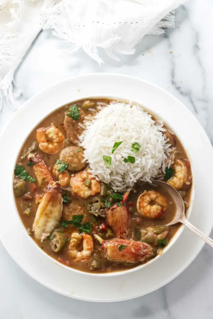 A bowl of seafood gumbo with a scoop of rice on top.