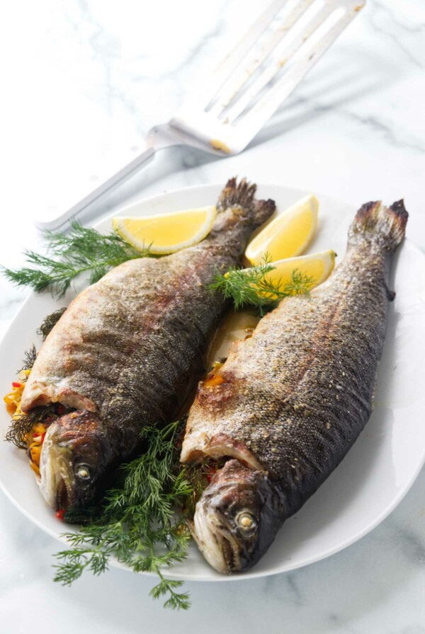 Two baked stuffed trout on a platter with lemon wedges and fresh dill.