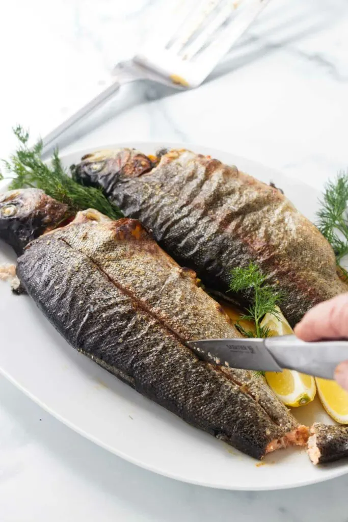 Two stuffed trout on a serving platter with a knife preparing to remove the trout spine bone.