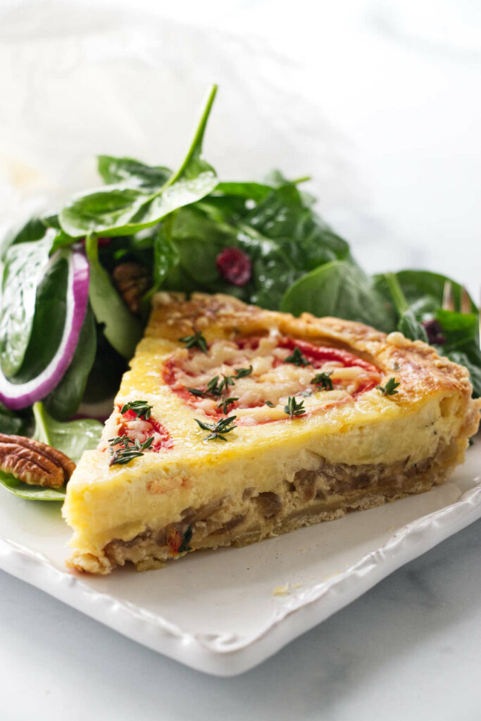 A slice of quiche on a plate with spinach salad.