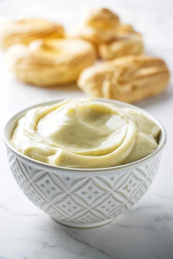 Vanilla pastry cream in a bowl with cream puffs in the background.