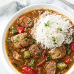 A bowl of sausage and chicken gumbo with a scoop of white rice on top.