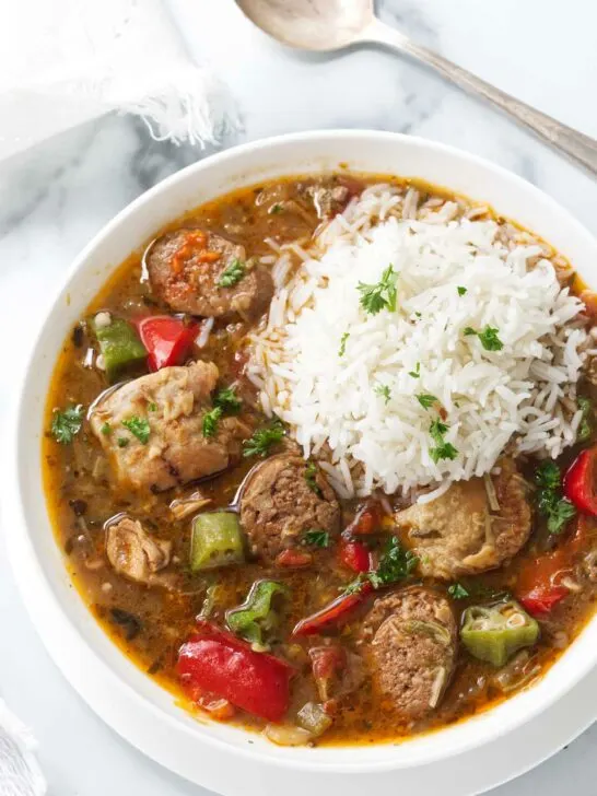 A bowl of sausage and chicken gumbo with a scoop of white rice on top.