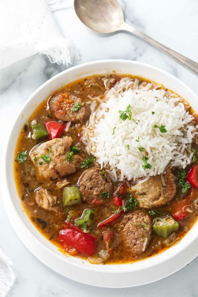 A bowl of sausage and chicken gumbo with a scoop of white rice on top.