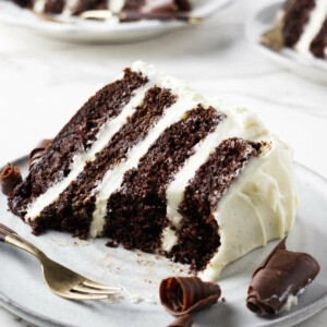 Slices of cream cheese frosting chocolate cake on three plates.