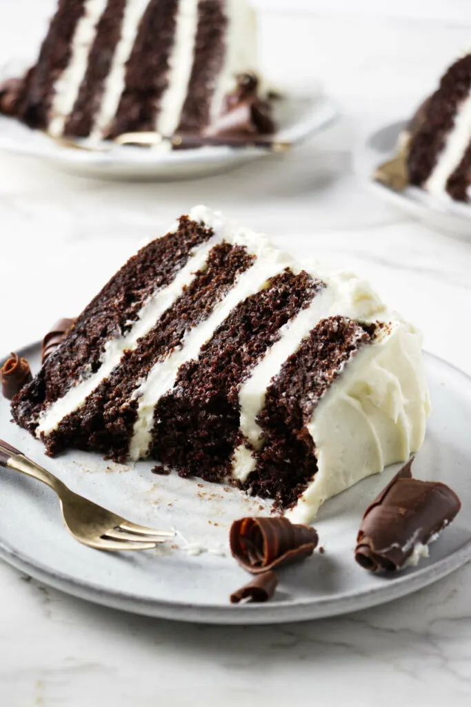 Slices of cream cheese frosting chocolate cake on three plates.