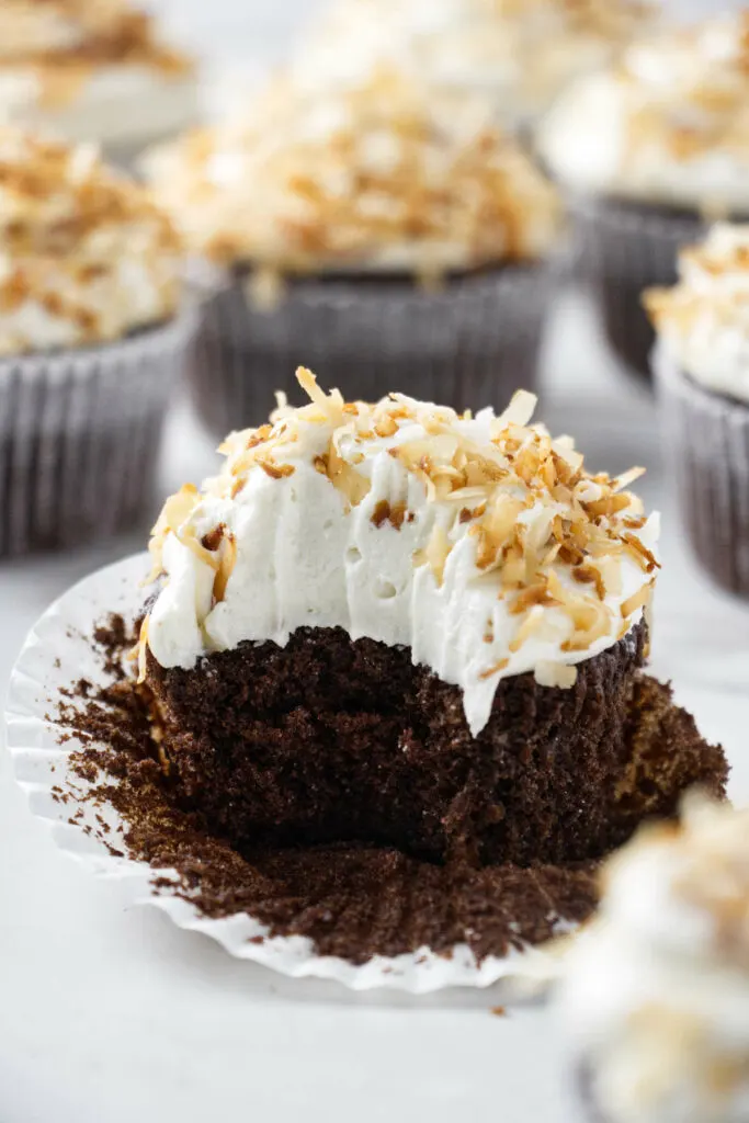 A partially eaten coconut chocolate cupcake with coconut buttercream.