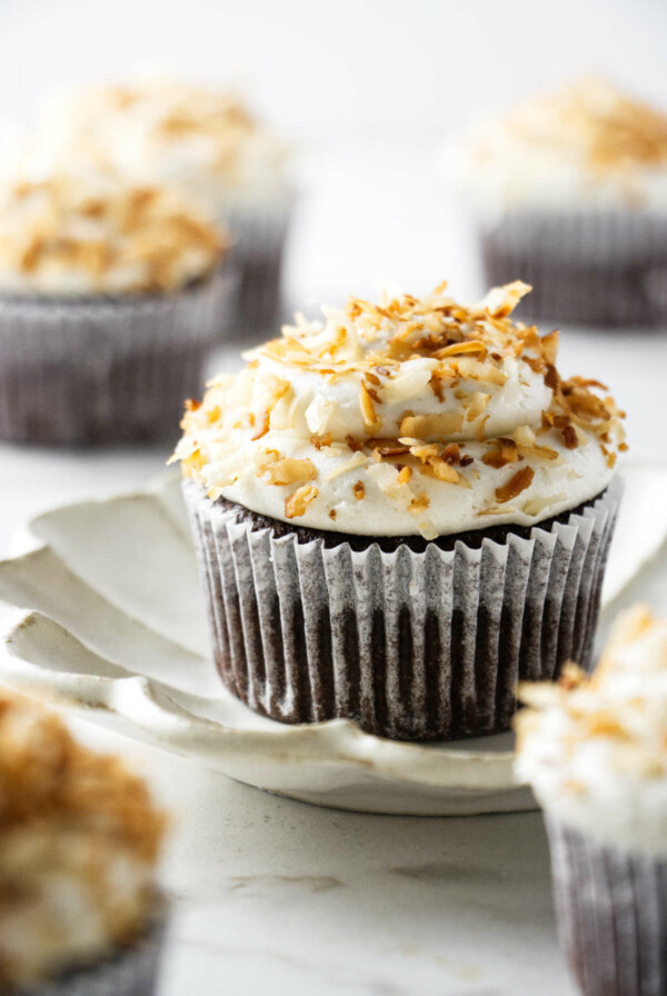 A coconut chocolate cupcake on a small plate with more cupcakes near by.