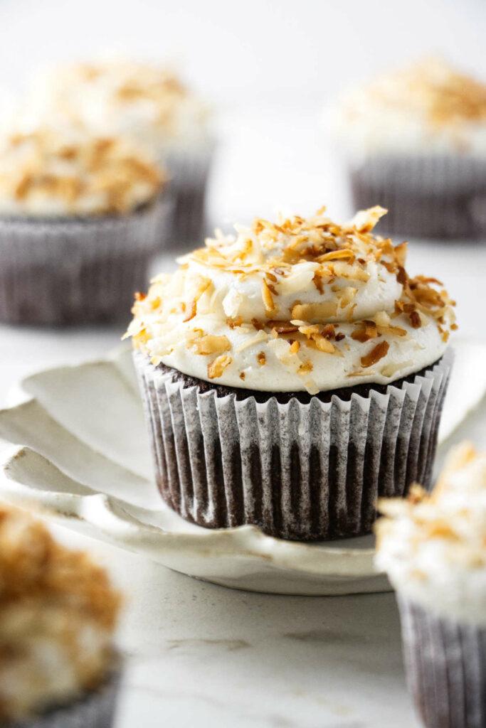 A coconut chocolate cupcake on a small plate with more cupcakes near by.