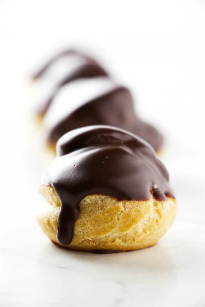 Several mini cream puffs topped with chocolate sauce.