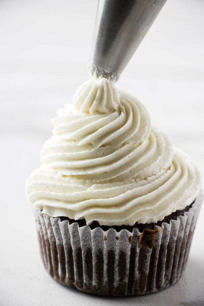 Piping coconut buttercream on a chocolate cupcake.