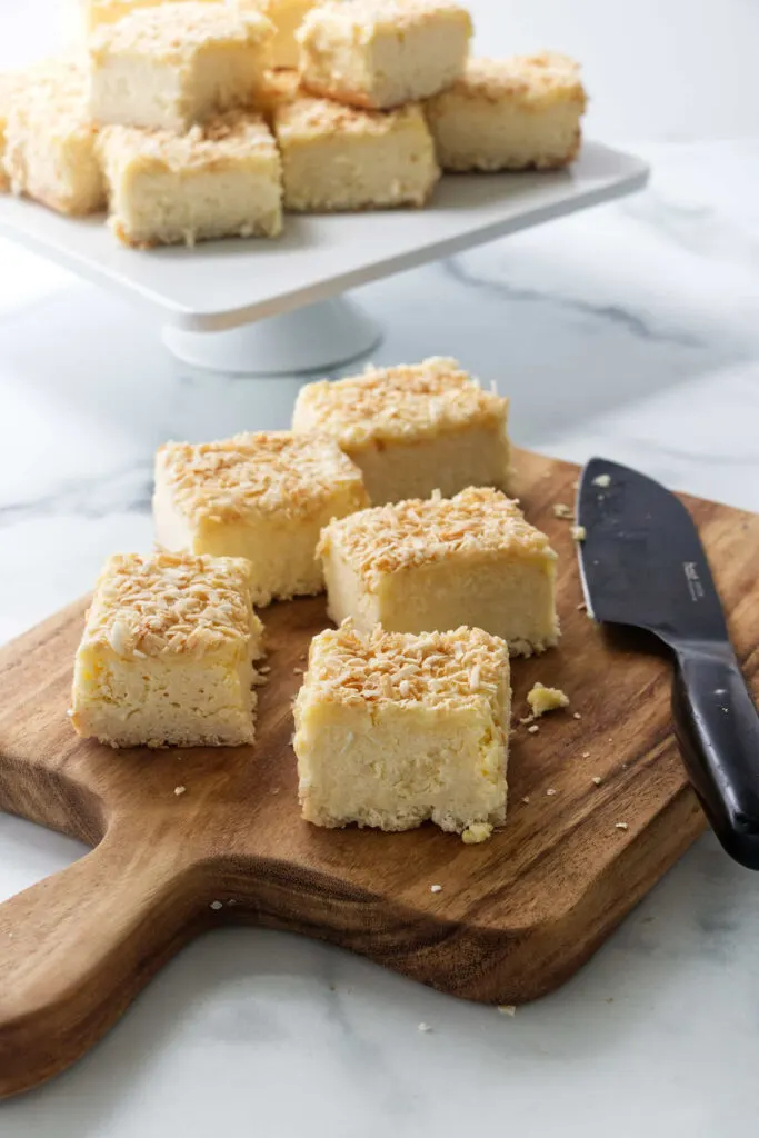 Slices of coconut cheesecake squares on a cutting board.