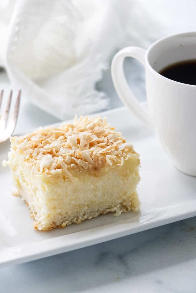 A coconut cheesecake bar on a plate with coffee.