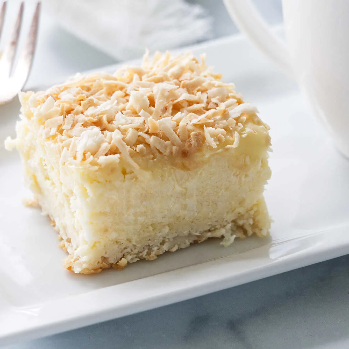 A creamy coconut cheesecake bar on a plate with coffee.