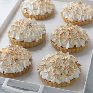 Mini lemon meringue tarts on a white tray.