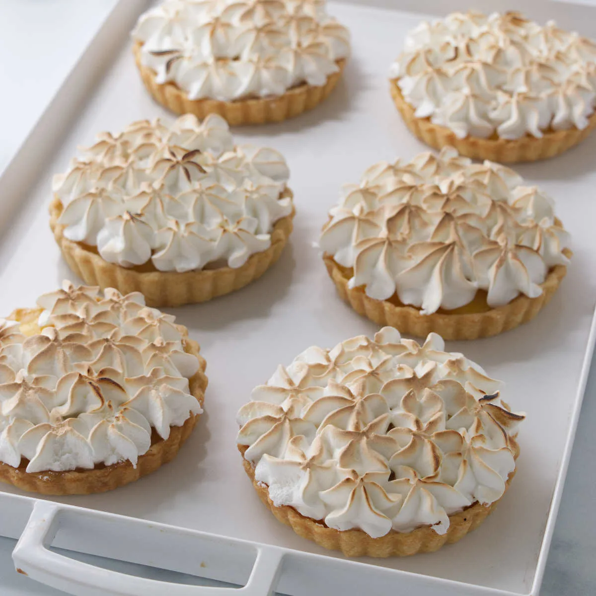 Mini lemon meringue tarts on a white tray.