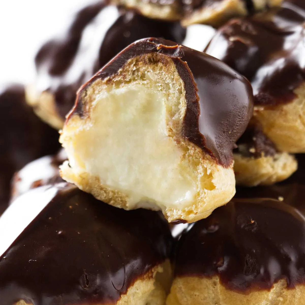 A stack of mini cream puff profiteroles filled with pastry cream and topped with chocolate sauce.