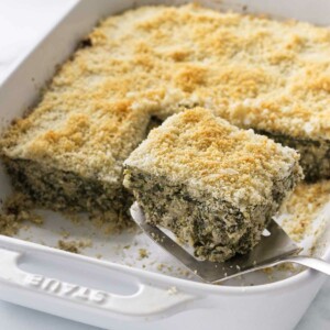 Removing a slice of spinach artichoke casserole with a spatula.