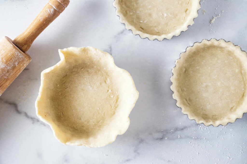 Placing pie dough in small tart pans.