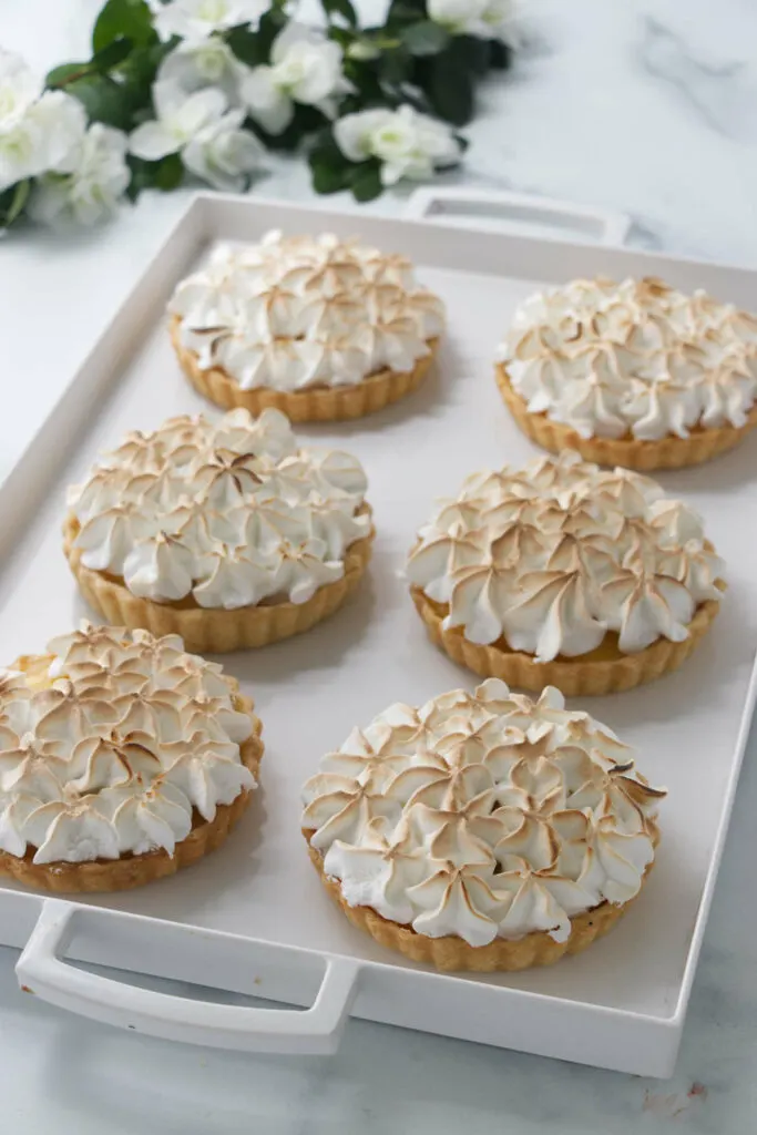 Six small lemon meringue tarts on a tray.