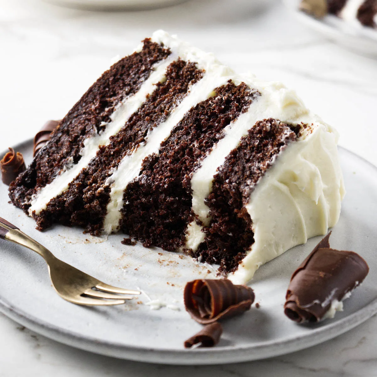 A cream cheese frosting chocolate cake on a plate with a fork and chocolate curls.