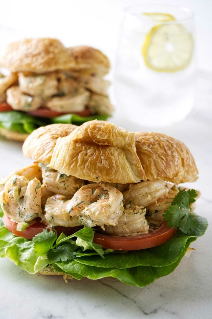 Two shrimp salad sandwiches with lettuce and tomato.