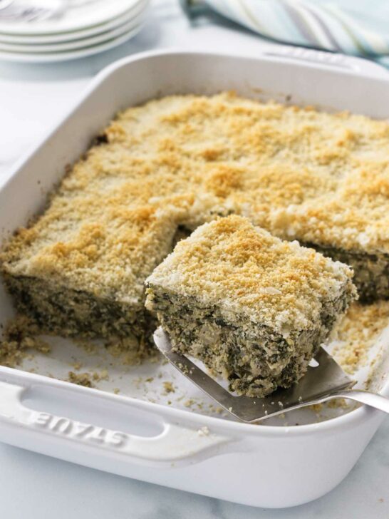 Spinach artichoke casserole being served with a spatula.