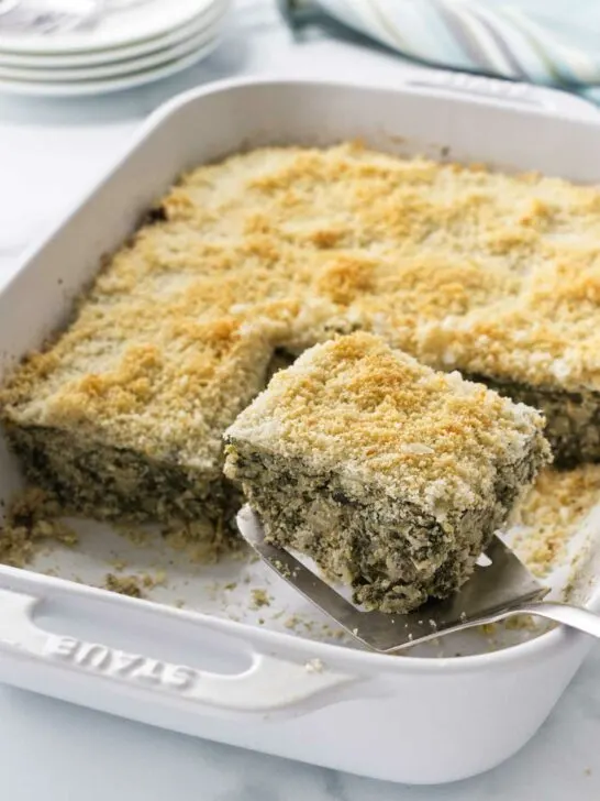 Spinach artichoke casserole being served with a spatula.