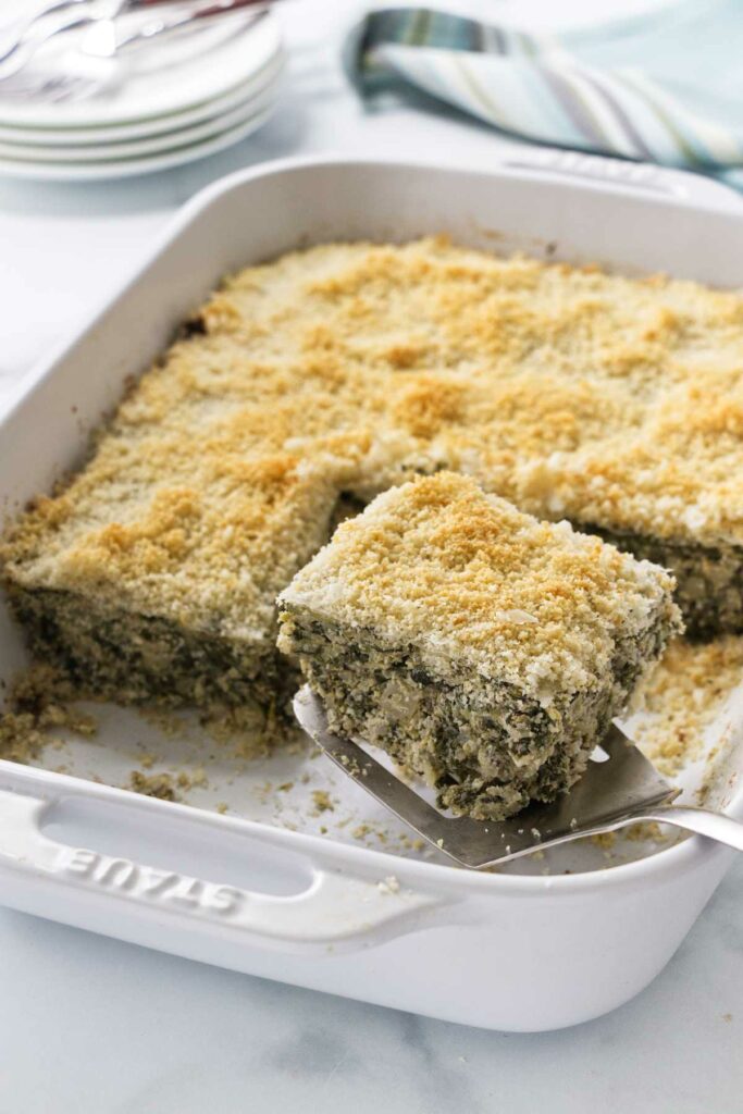 Spinach artichoke casserole being served with a spatula.