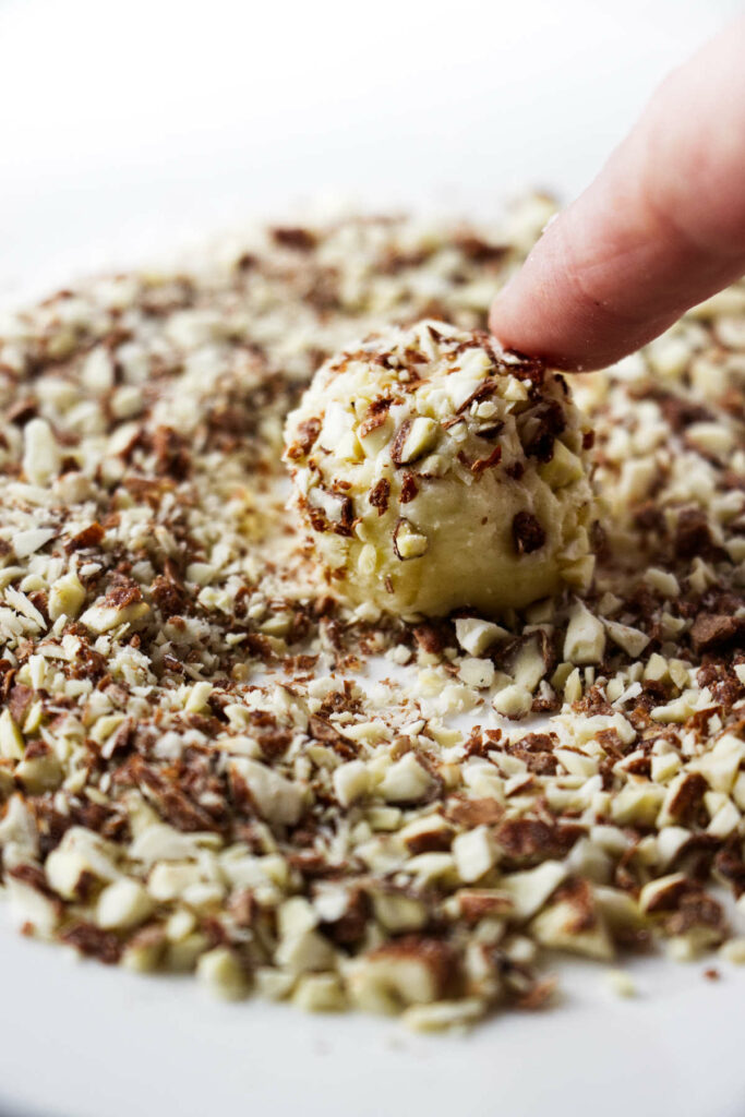 Rolling a white chocolate ganache truffle in chopped nuts.