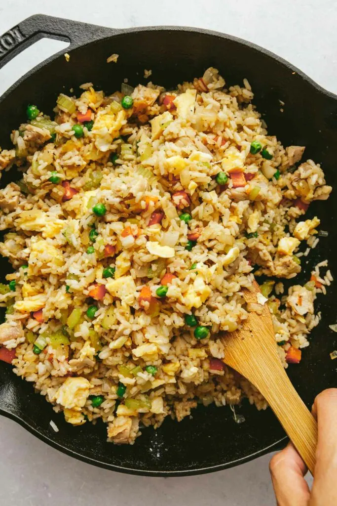 Chicken fried rice in a skillet with a wooden spoon.