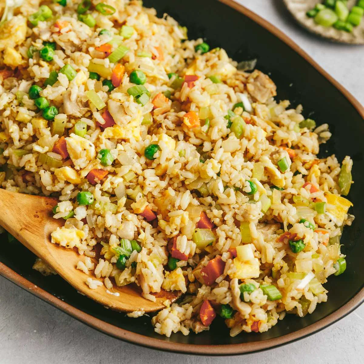 A bowl of chicken fried rice next to some chopped scallions.