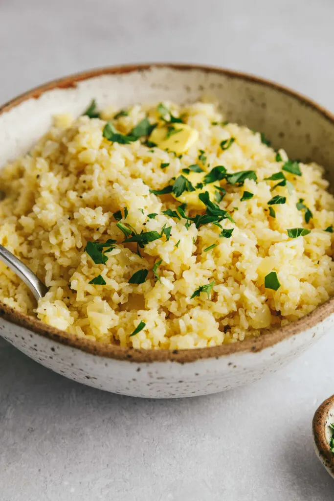 A bowl of buttery garlic rice with herbs on top.