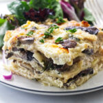 A slice of mushroom lasagna on a plate with green salad.