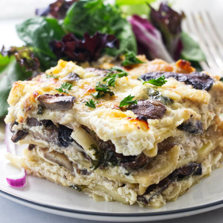A serving of mushroom lasagna on a plate with side salad and fork.