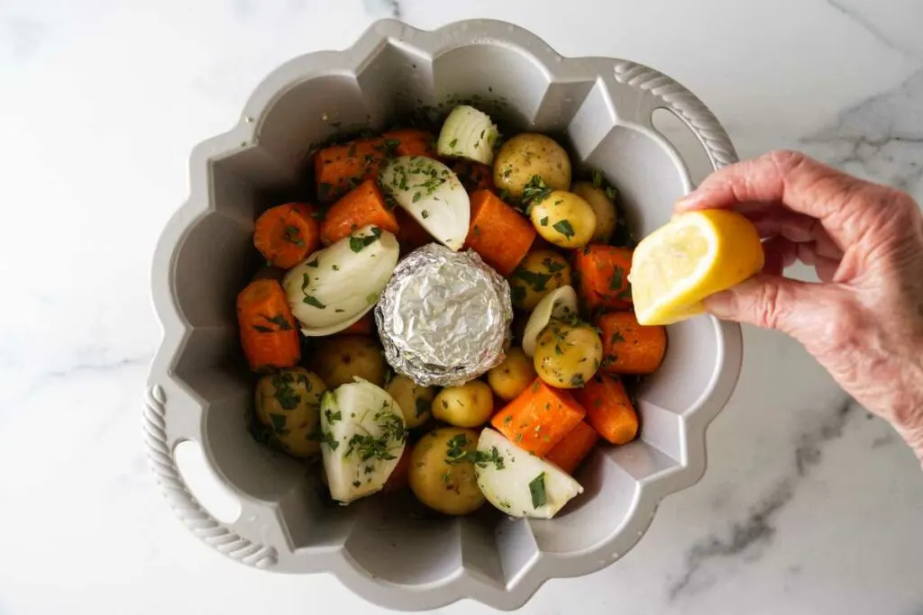 A bundt pan with seasoned vegetables, squeezing a lemon on the vegetables.