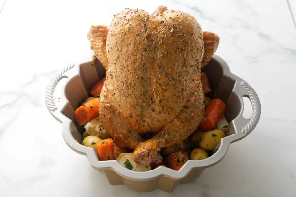 A chicken propped on top of veggies in a pan.