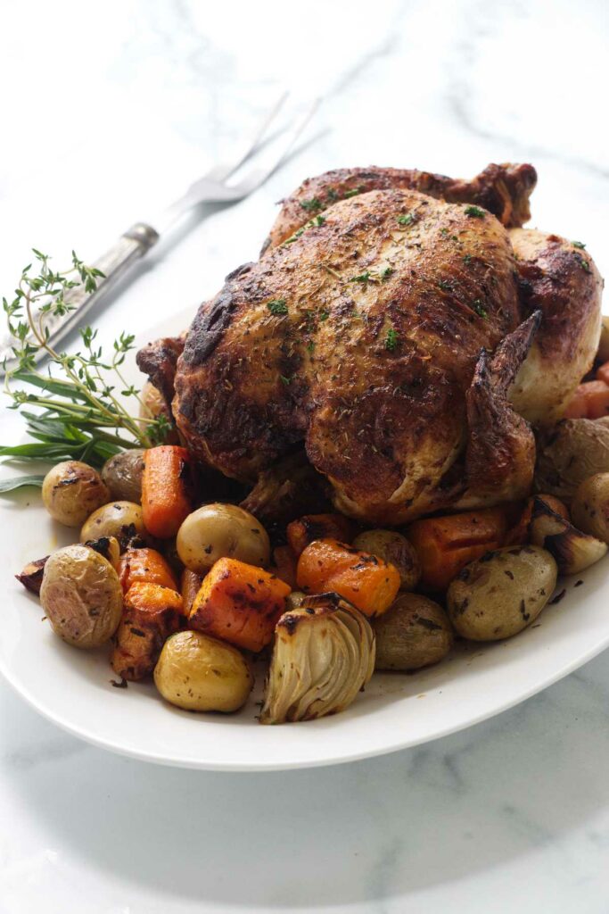 Platter with the roasted chicken and vegetables. A serving fork to the left.