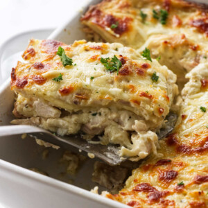 Scooping a slice of chicken alfredo lasagna out of a casserole dish.