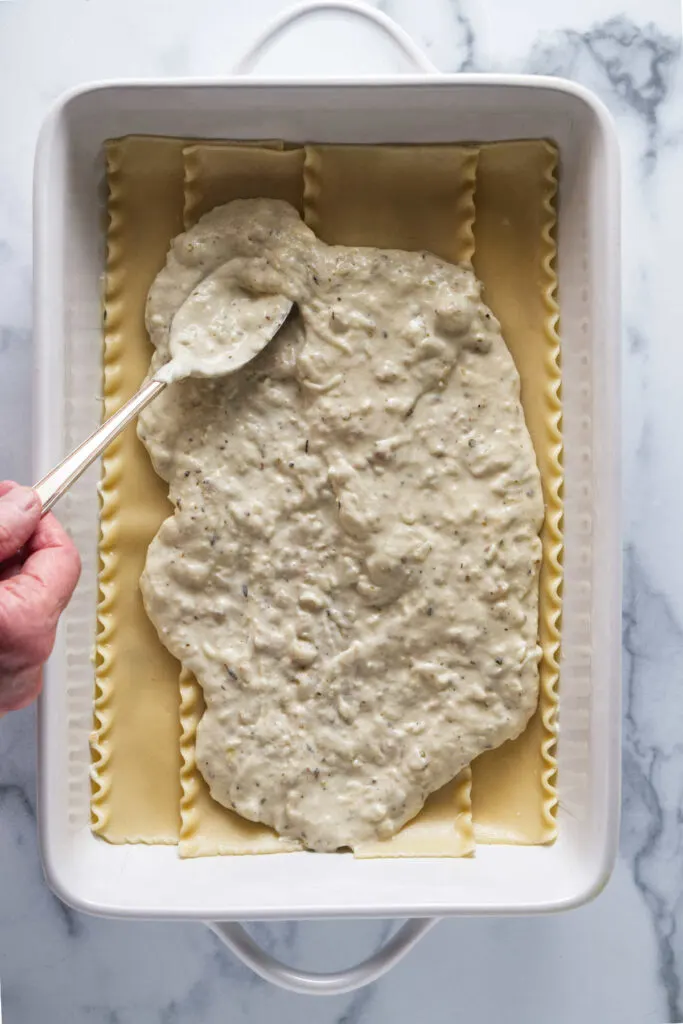 Spreading white sauce over lasagna noodles.