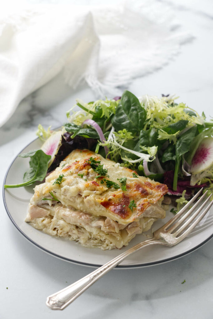 A serving of chicken lasagna on a plate with salad.