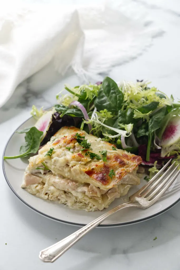 A serving of chicken lasagna on a plate with salad.