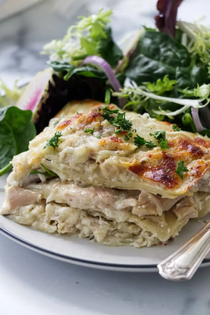 A slice of chicken alfredo lasagna on a plate with salad.