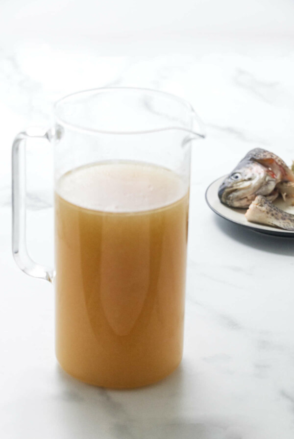 Pitcher of homemade fish broth and a saucer in the background with fish head/tail.