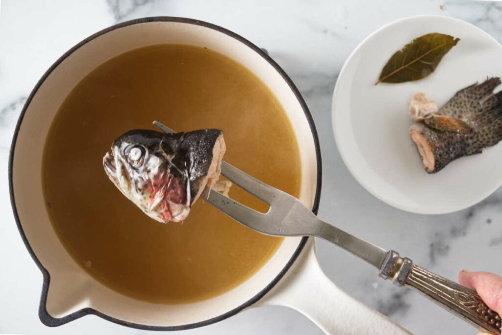 Lifting the fish head from the broth. Fish tail and bay leaf on a small saucer to the right.