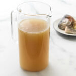 Pitcher of homemade fish broth. Saucer in the background with fish head and tail.